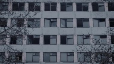 Çok katlı boş bir binanın dış cephesi. Kırık çerçeveler ve pencere camları, genel ıssızlık.