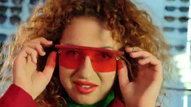 Mujer con gafas sacude pelos rizados y guiños en el estudio — Vídeo de stock
