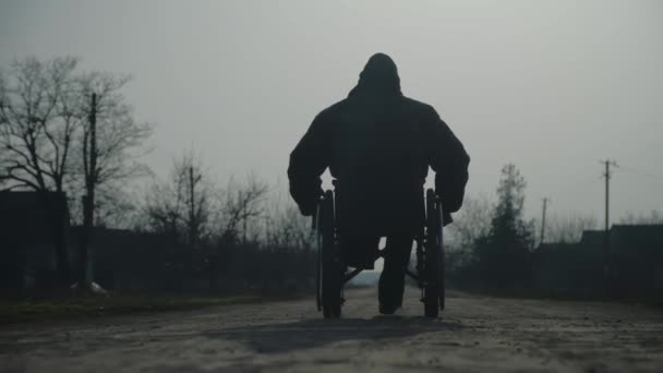 Чоловік-ампутат у теплій куртці їде на інвалідному візку на наземній дорозі — стокове відео