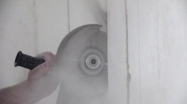 İşçi evde toz bulutu içinde duvarı dairesel testereyle kesiyor
