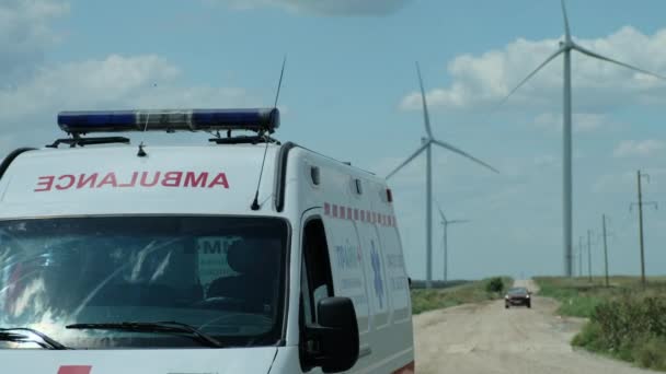 Stojący ambulans na wiejskiej drodze przed turbinami wiatrowymi — Wideo stockowe