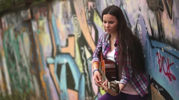La chica con la guitarra contra una pared con graffiti — Vídeos de Stock