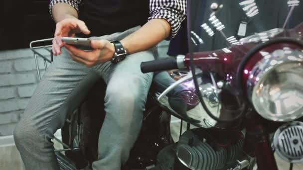 Молодой человек сидит на мотоцикле и переворачивает страницы в телефоне — стоковое видео