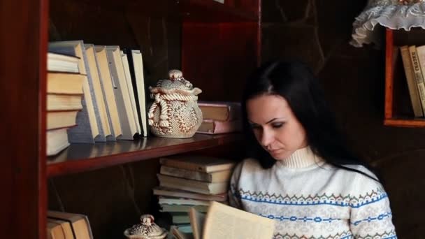 A jovem perto de uma estante de livros lendo um livro — Vídeo de Stock