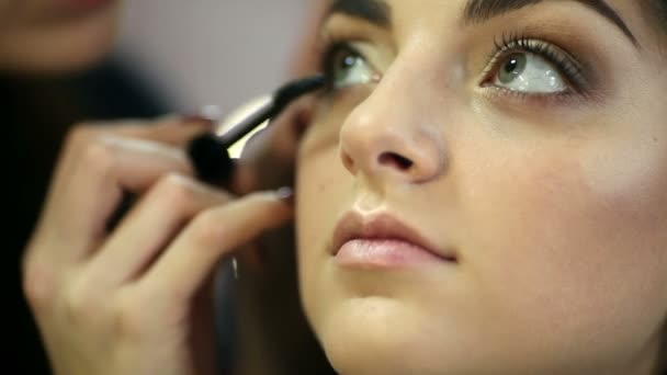 Una mujer guapa con maquillaje aplicado por un maquillador . — Vídeos de Stock