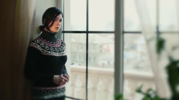 Ένα κορίτσι σε ένα πουλόβερ δίπλα στο παράθυρο. — Αρχείο Βίντεο