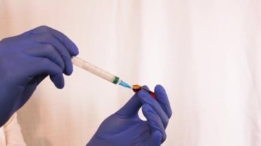 Mavi eldivenli bir doktor şırıngaya ilaç koyuyor. Belki de koronavirüse karşı bir aşıdır.