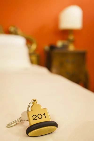 Chave da sala de hotel deitada na cama com chaveiro Imagem De Stock