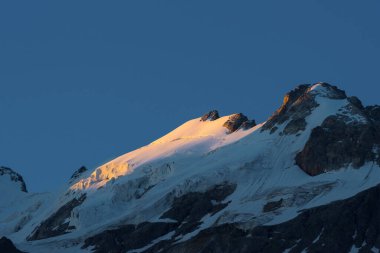 Kayalık dağın tepesindeki buzullar ilk ışıkla aydınlatılıyor.