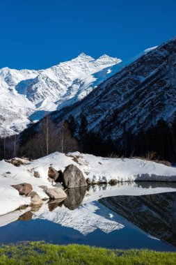 Karlı Kogutai dağları küçük dağ gölü yüzeyine yansıdı. Kabardino-Balkaria, Elbrus, Rusya.