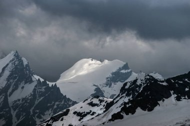 Doğa arka planı - Elbrus bölgesindeki karlı Rus Kafkasya dağlarının üzerindeki karanlık fırtınalı gökyüzü.