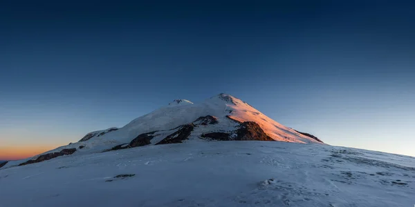 Dağ 'ın panoramik manzarası Elbrus güneş doğarken güney yamacından çıkar. Prielbrusie Ulusal Parkı, Kabardino-Balkaria, Rusya.
