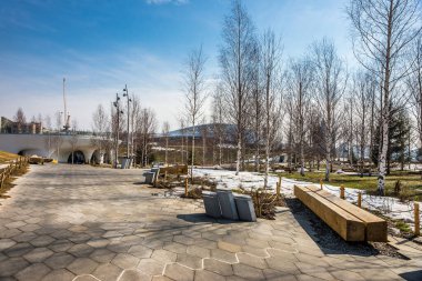 Zaryadye Park manzarası ilkbaharın başlarında güneşli bir gün: bir huş ağacında ahşap banklar ile Amphitheater ve Kotelnicheskaya Embankment Binası karşı.