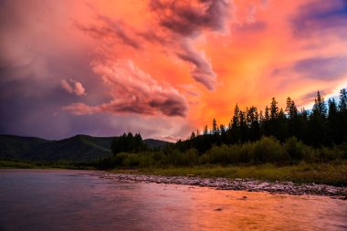 Sibirya dağlarındaki Balyiktyig nehri kıyısındaki Taiga ormanının üzerinde renkli bulutlu gün batımı gökyüzü.