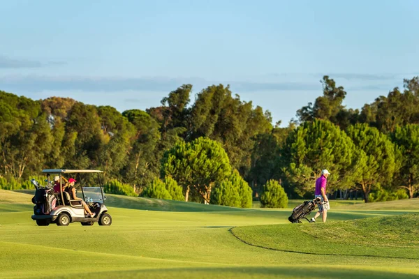 ANTALYA, TURKEY - 29 Eylül 2014: Golf arabasında tanımlanamayan bir çift ve golf çantalarıyla çim yolunda yürüyen bir adam. Türkiye 'nin Antalya kentinde golf sahası