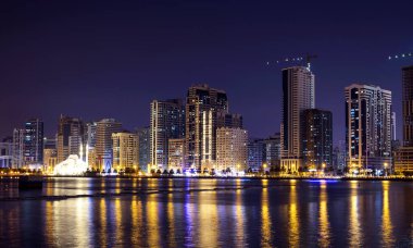 Sharjah, BAE, 2 Aralık 2020. Aydınlatılmış gökyüzü kazıyıcılarının panoramik görüntüsü ve ünlü Al Noor camii Al Majaz rıhtım şerifi, BAE 'de yakalanan suda güzel yansımaları gösteriyor..