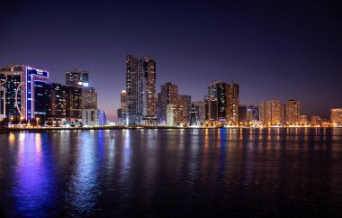 Sharjah, BAE - 2 Aralık 2020. Aydınlatılmış gökyüzü kazıyıcılarının panoramik görüntüsü Al Majaz rıhtım şerifi, BAE 'de yakalanan suda güzel yansımaları gösteriyor..