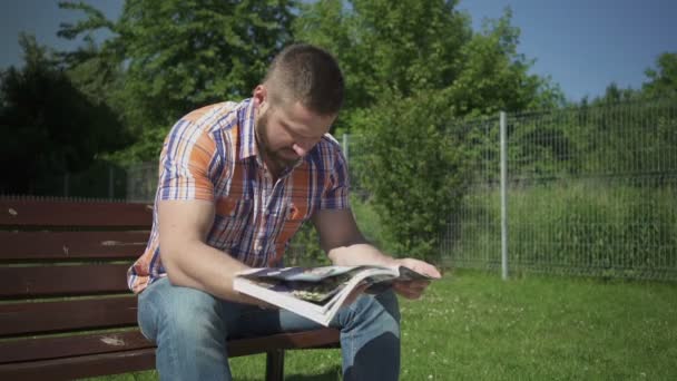 Hombre está leyendo revista en banco de madera . — Vídeos de Stock