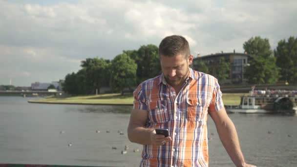 Hombre navegando teléfono inteligente por el río . — Vídeos de Stock