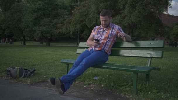 Hombre navegando por teléfono inteligente, sentado en la fosa de madera, toma de la cacerola . — Vídeos de Stock