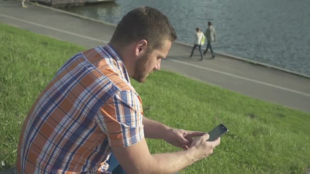 Mann surft mit Smartphone am Fluss. — Stockvideo