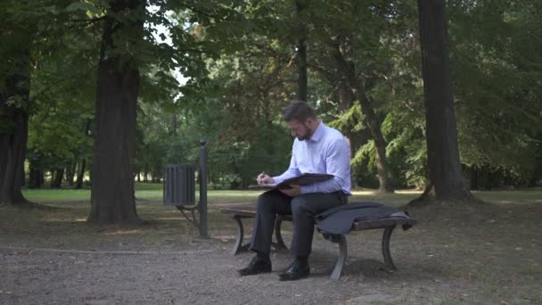 Επιχειρηματίας τελειώνει εργασίας με έγγραφα στο πάρκο και πηγαίνει μακριά. — Αρχείο Βίντεο