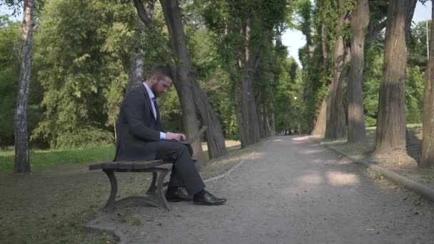 Biznesmen pracy na laptopie, siedząc na ławce w parku. — Wideo stockowe