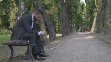 Park ahşap bankta oturmuş smartphone tarama Busienessman.