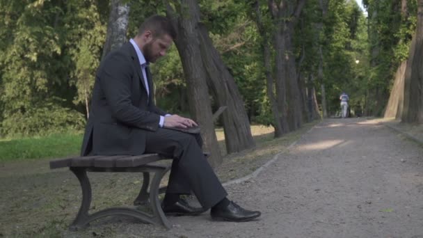 Uomo d'affari che lavora sul computer portatile, seduto sulla panchina nel parco, pan e tilt shot . — Video Stock