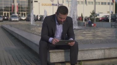 Tablet tarama, duvarda oturan işadamı. Pan çekim.