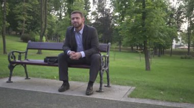 İşadamı oturan ve yuvarlak bakan, ahşap bankta oturan.