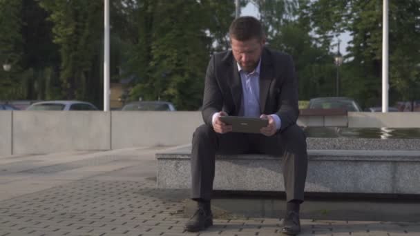 Zakenman zittend op de muur, surfen tablet, pan schot. — Stockvideo