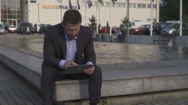 Zakenman browsing tablet, zittend op de muur. — Stockvideo