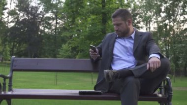 Busienessman Park, pan atış tahta bankta oturmuş smartphone tarama.