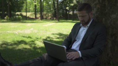 Dizüstü bilgisayar üzerinde çalışan işadamı telefon görüşmesine cevap veriyor. Pan atış.