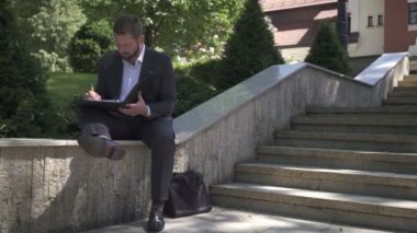 İşadamı belgelerle çalışıyor, duvarda oturuyor. Pan atış.