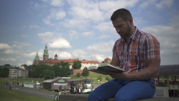 Człowiek czytanie książki na ścianie nad rzeką. — Wideo stockowe