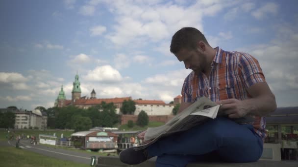 Mann liest Zeitung an der Wand am Fluss. — Stockvideo