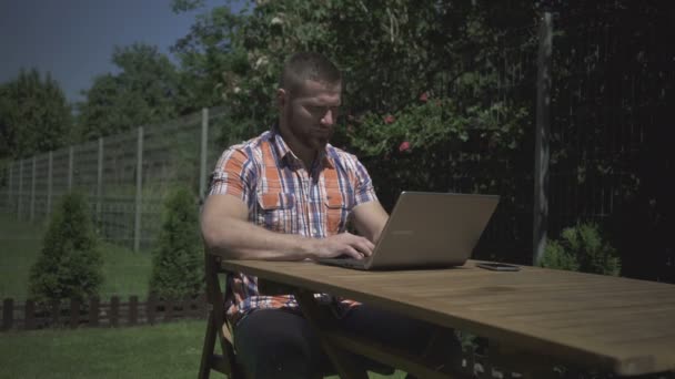 Uomo seduto in giardino e digitare sul computer portatile . — Video Stock