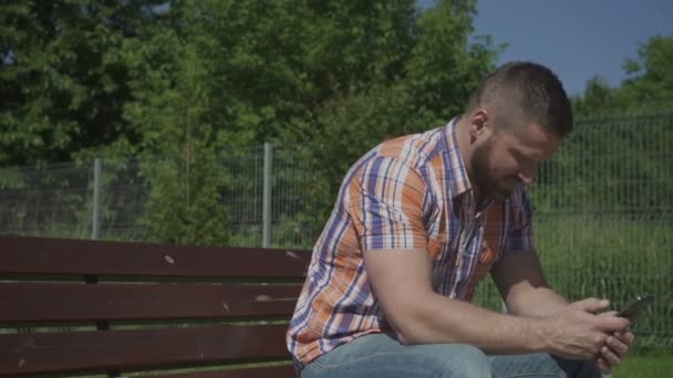 Man browsing smartphone on wooden bench, pan shot. — Stock Video