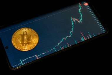 Şifreli para birimi Altın Bitcoin siyah arka planda izole edilmiş. Cep telefonunun önündeki Bitcoin değeri olan bozuk para fotoğrafı. Engelleme teknolojisi, bitcoin madencilik kavramı.
