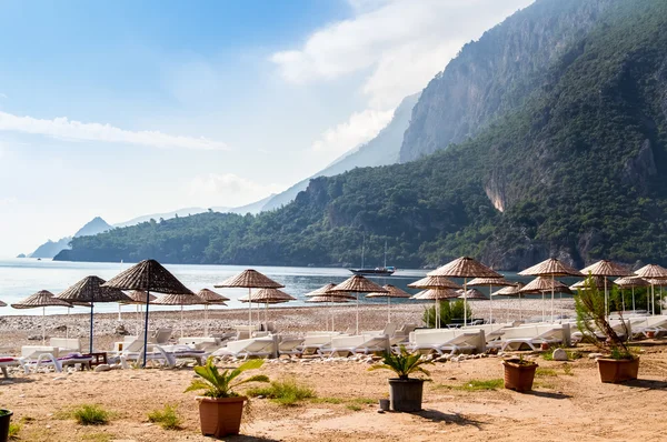 Çıralı plaj üzerinde thatched şemsiye altında güverte sandalyeleri.