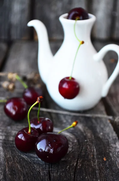 A pair of cherries on the old wooden table with a white jug on a background — Stock Photo, Image