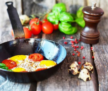 Domates ve fesleğen eski ahşap masa üzerinde siyah tavada omlet