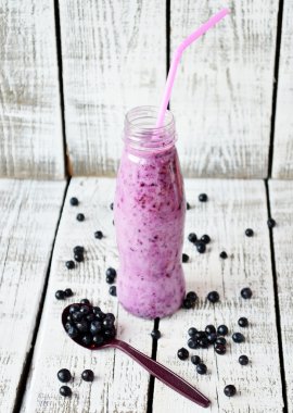 Beyaz ahşap zemin üzerinde pembe sopayla şişede Blueberry smoothie