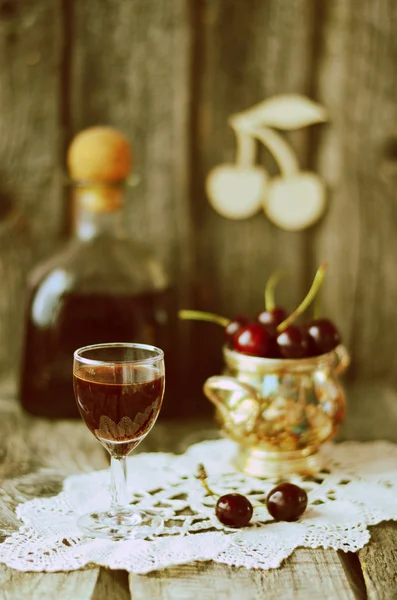 Cherry liquor in the little glasses and big bottle on the old wooden background with sepia effect — Stock Photo, Image