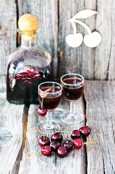 Cherry liquor in the little glasses and big bottle on the old wooden background