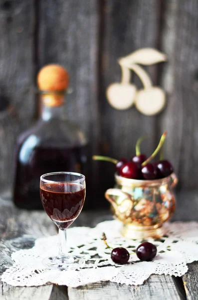 Cherry liquor in the little glasses and big bottle on the old wooden background — Stock Photo, Image