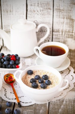 Porridge with blueberry and cup of tea on the vintage napkin on the white wooden background, Russian style spoon in desaturated tone, moody lighting