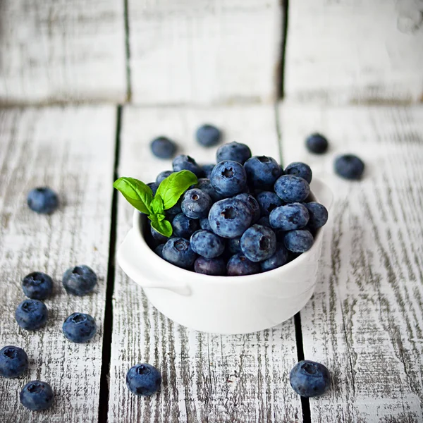 Vit skål med blåbär på den vita träbord med basilika blad — Stockfoto